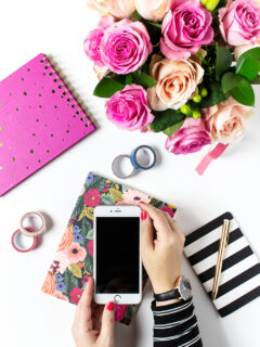 Holding iphone over planner on desk with flowers, tape, pens, and notebooks.